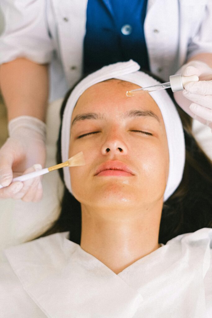 pexels-photo-5069432-5069432 Top view skilled female cosmetologist in uniform and gloves applying essential oil on young woman face skin while working in contemporary spa center