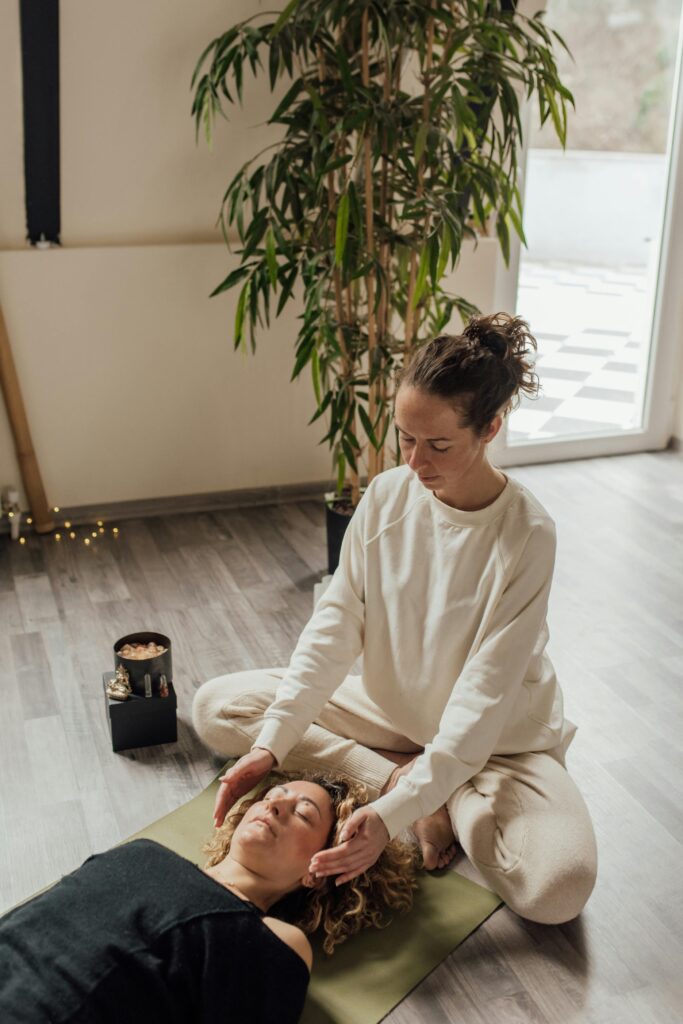 pexels-photo-6998280-6998280 A calming scene depicting a woman practicing Reiki therapy on another woman lying on a yoga mat indoors.